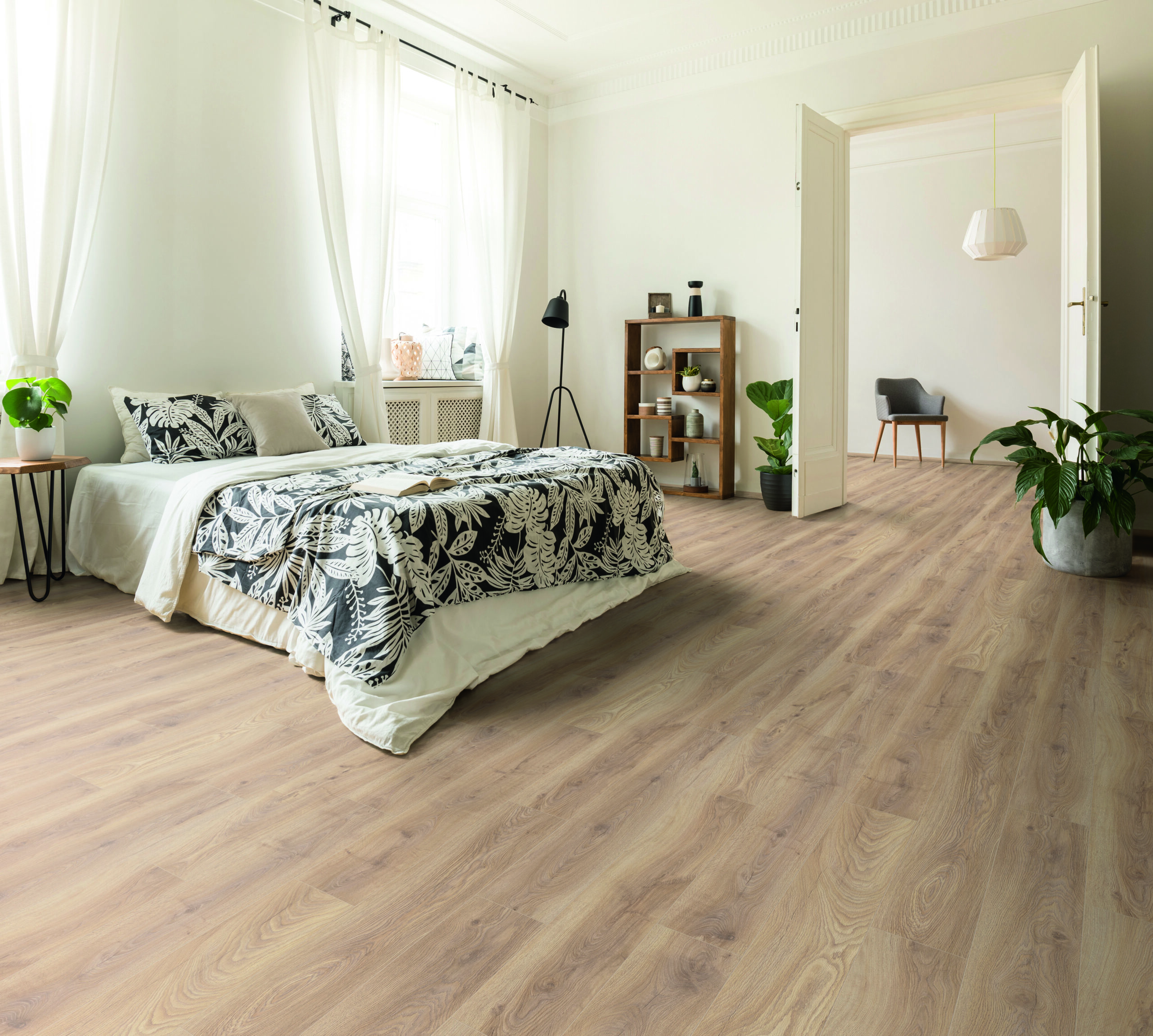Stylish apartment interior with white walls and herringbone wooden floor. A view from a bedroom with a big bed to another room with an armchair. Real photo.